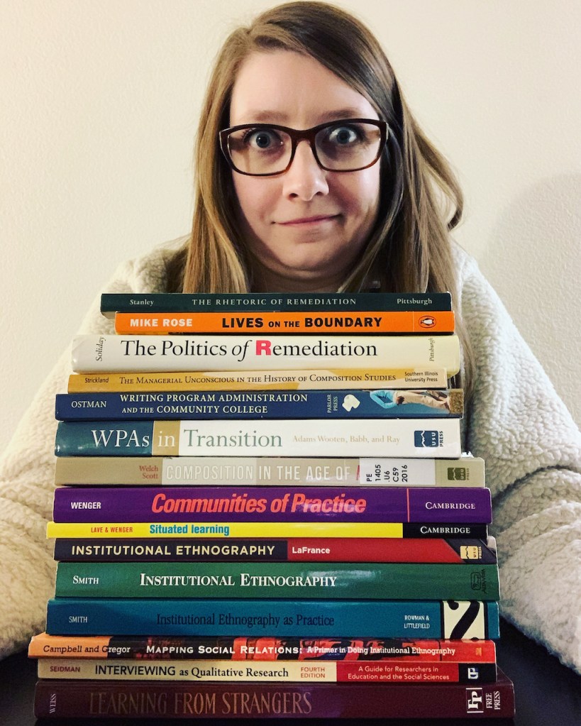 I picture of a brown haired woman with glasses sitting behind a stack of books. 
